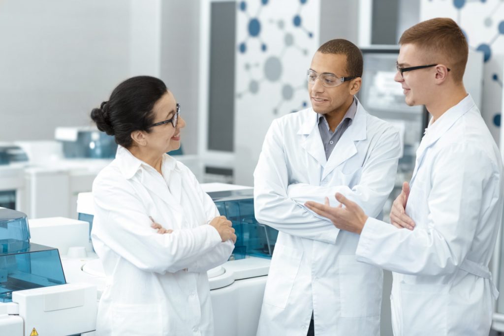 A female scientist speaking to two male scientists in a clinical lab.