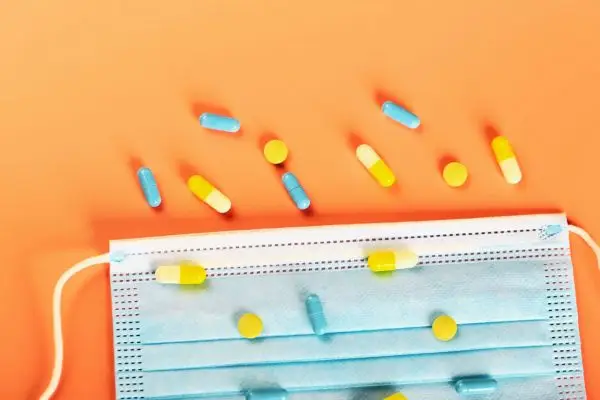 A blue face mask on an orange background covered with vitamin d supplements