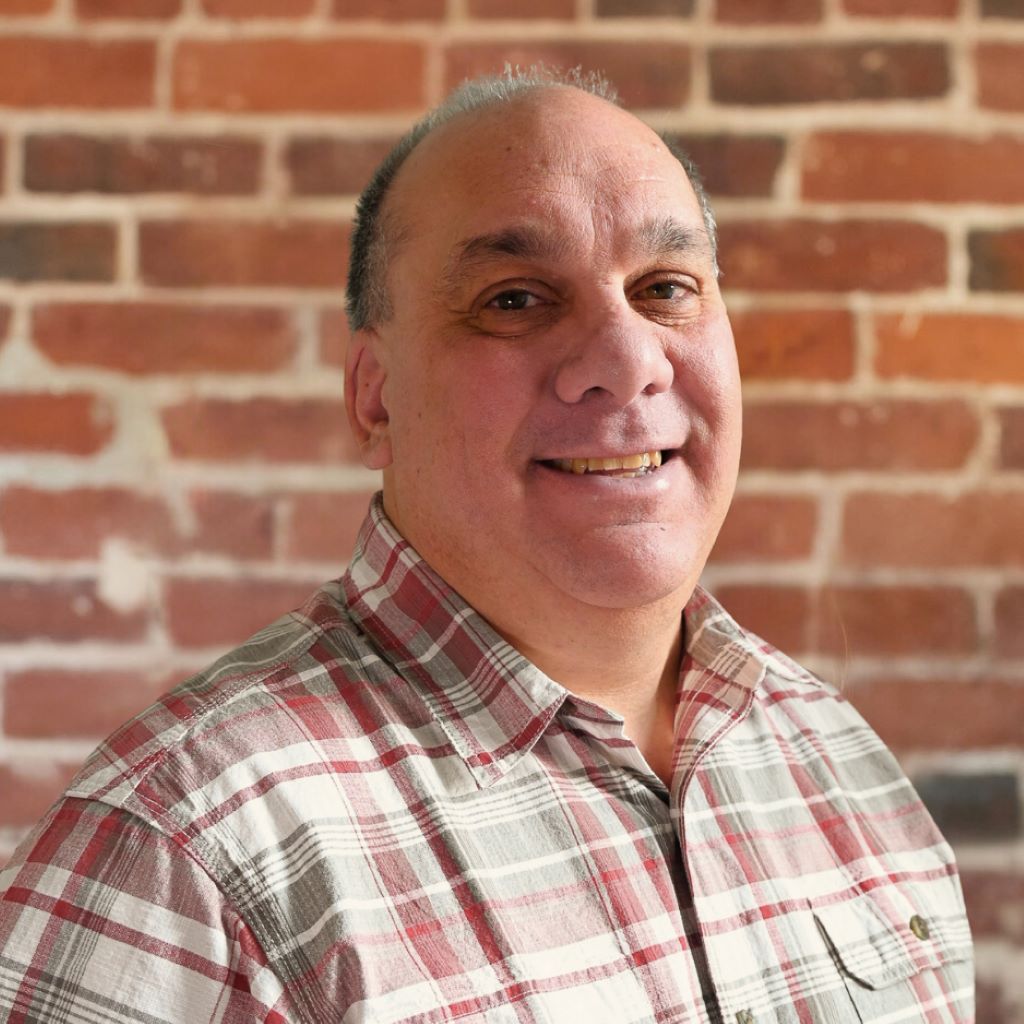 A headshot of IDK, Inc.'s Logistics Manager, Darryl Hicks, in front of a brick wall.