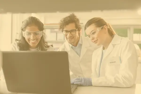 Three lab technicians gathered in front of a laptop watching the screen.