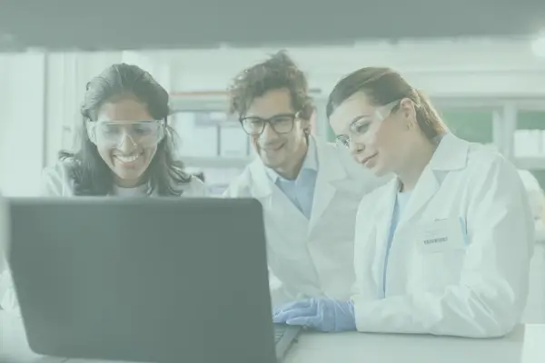Three lab technicians gathered in front of a laptop watching the screen.