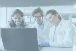 Three lab technicians gathered in front of a laptop watching the screen.