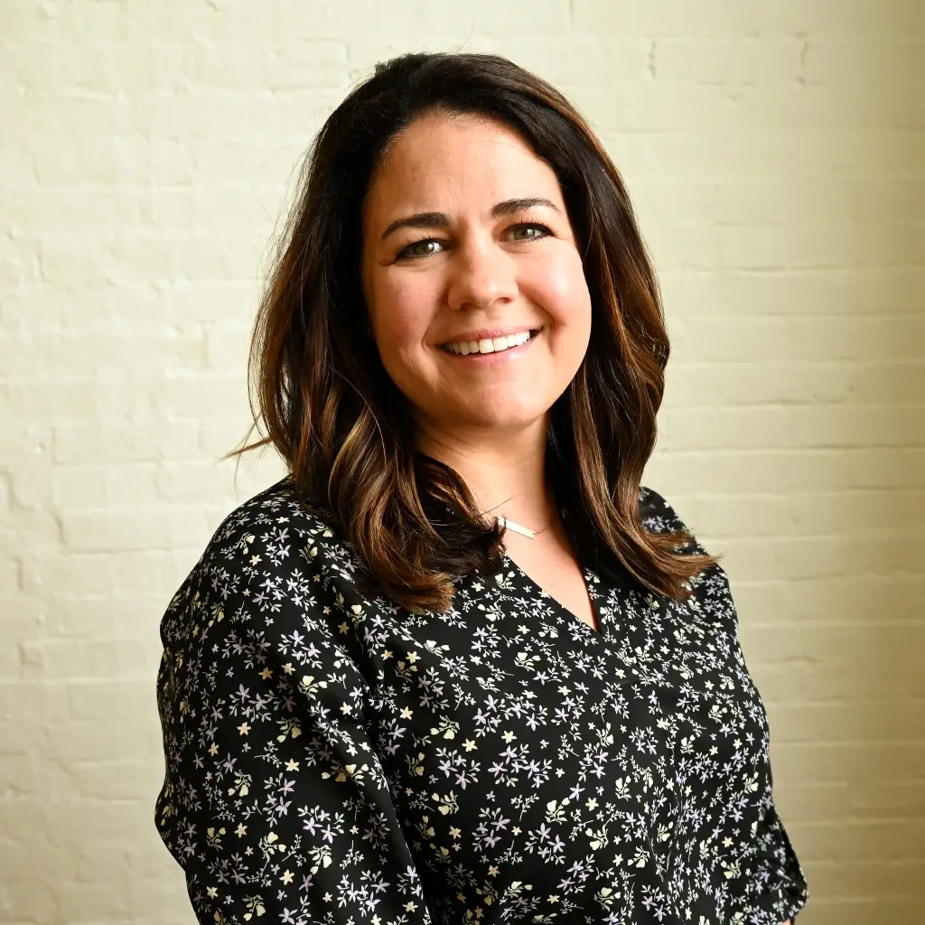 Alison Hall, Executive Administrator at Immundiagnostik, Inc., smiling in front of a white brick wall.