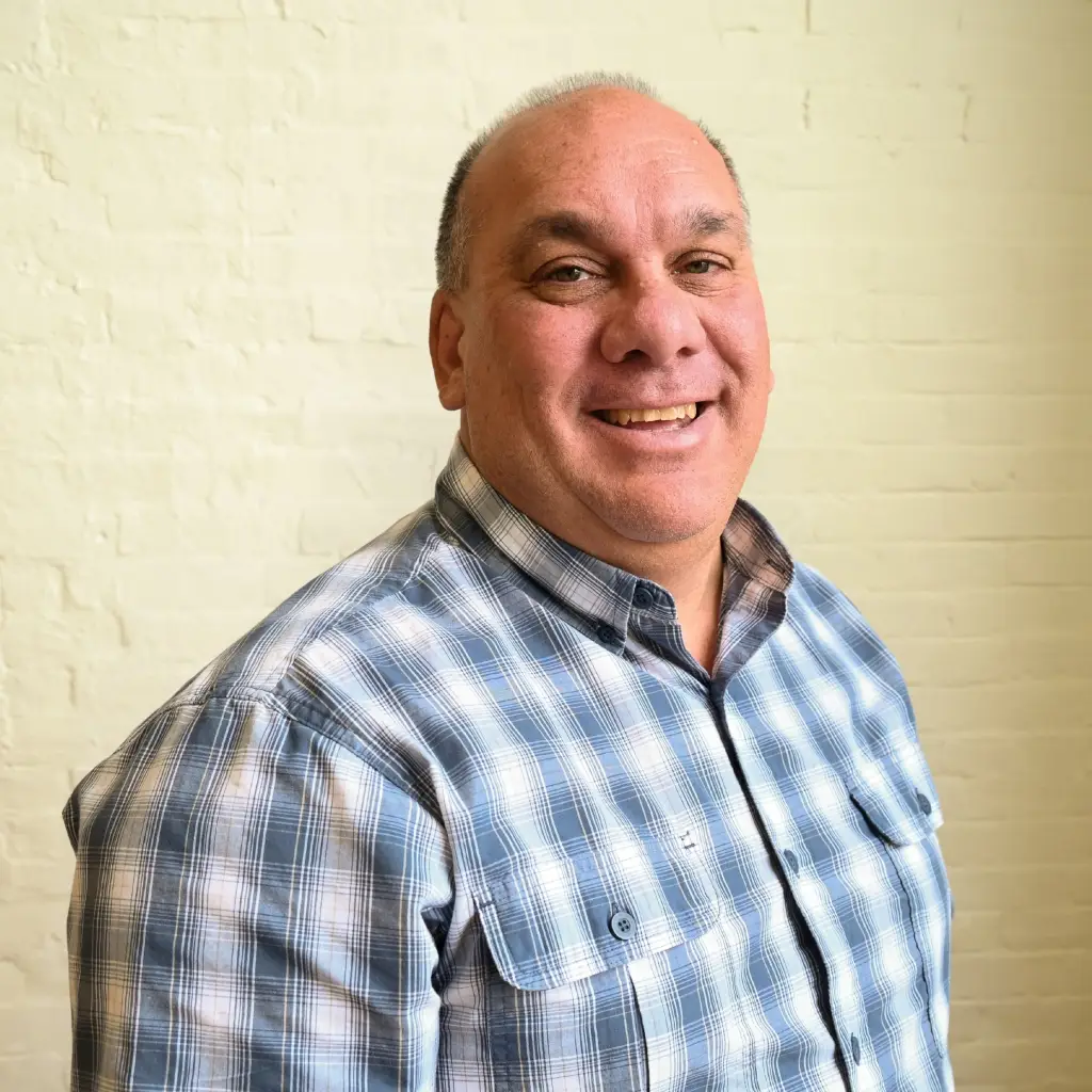 Darryl Hicks, Logistics Manager at Immundiagnostik, Inc., smiling in front of a white brick wall.