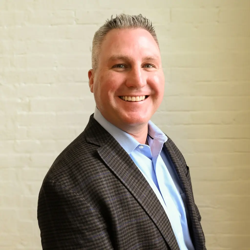 Derek Abbott, Regional Sales Director NW & SE at Immundiagnostik, Inc., smiling in front of a white brick wall.