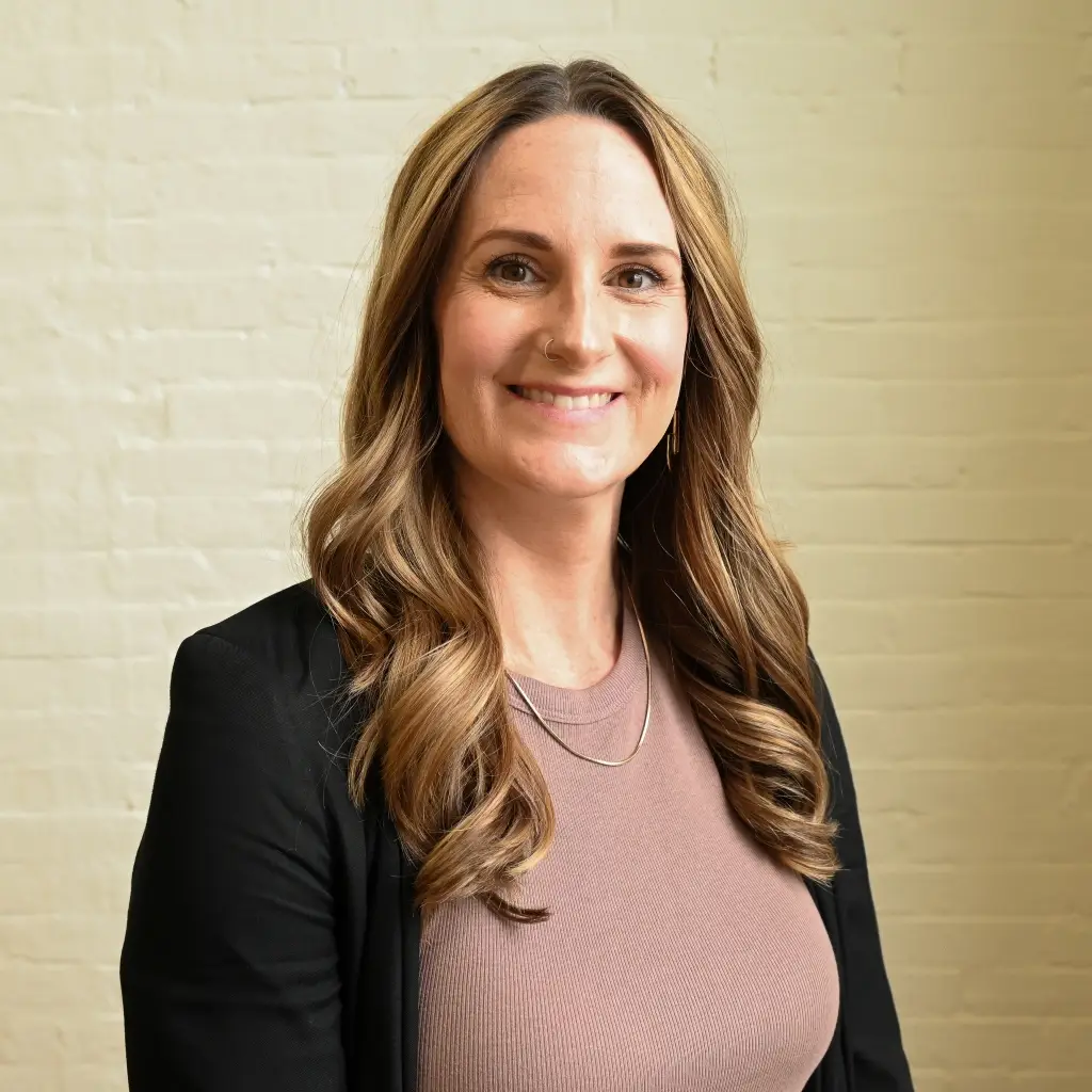 Noelle Hurley, Marketing Communications Manager at Immundiagnostik, Inc., smiling in front of a white brick wall.
