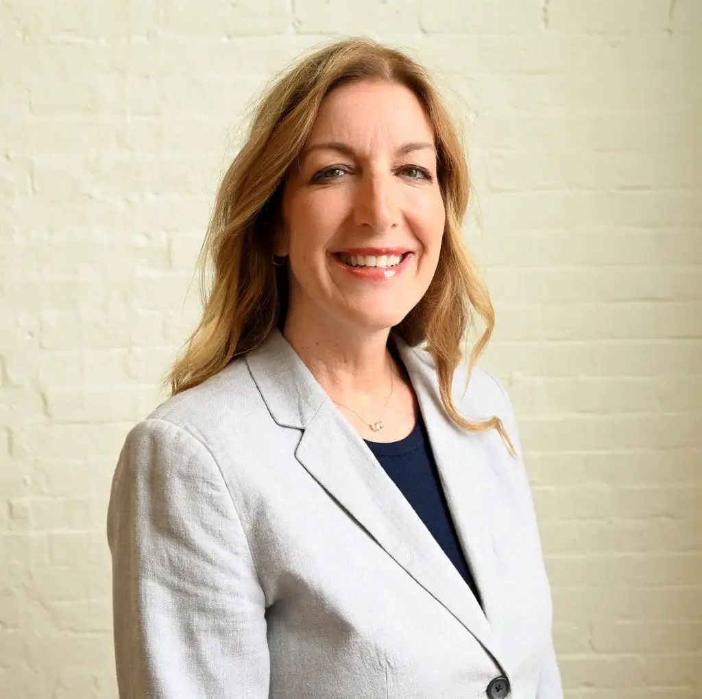 Jen Mayes, Chief Commercial Officer at Immundiagnostik, Inc., smiling in front of a white brick wall.