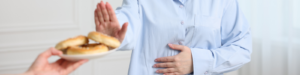 Someone putting their hand out to stop another person from giving them a plate of gluten-containing bread, while they clutch their stomach with their other hand.