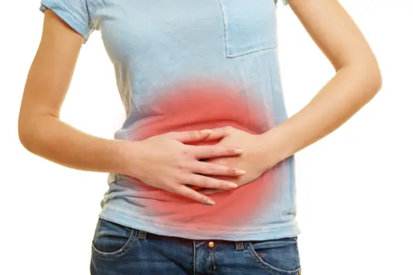 A woman in a blue t-shirt clutching a red circle highlighted on her stomach, indicating celiac disease symptoms.